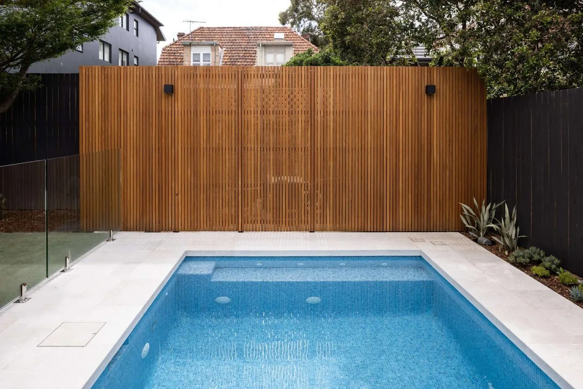 Mosaic-tiled pool, limestone surrounds and timber-battened privacy wall with glass fencing | Refined Group