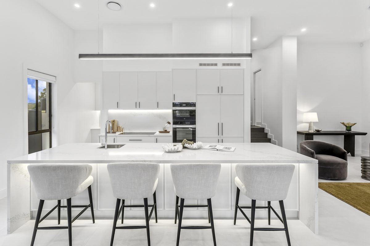White kitchen with marble island bench and upholstered stools in a Refined Group custom home