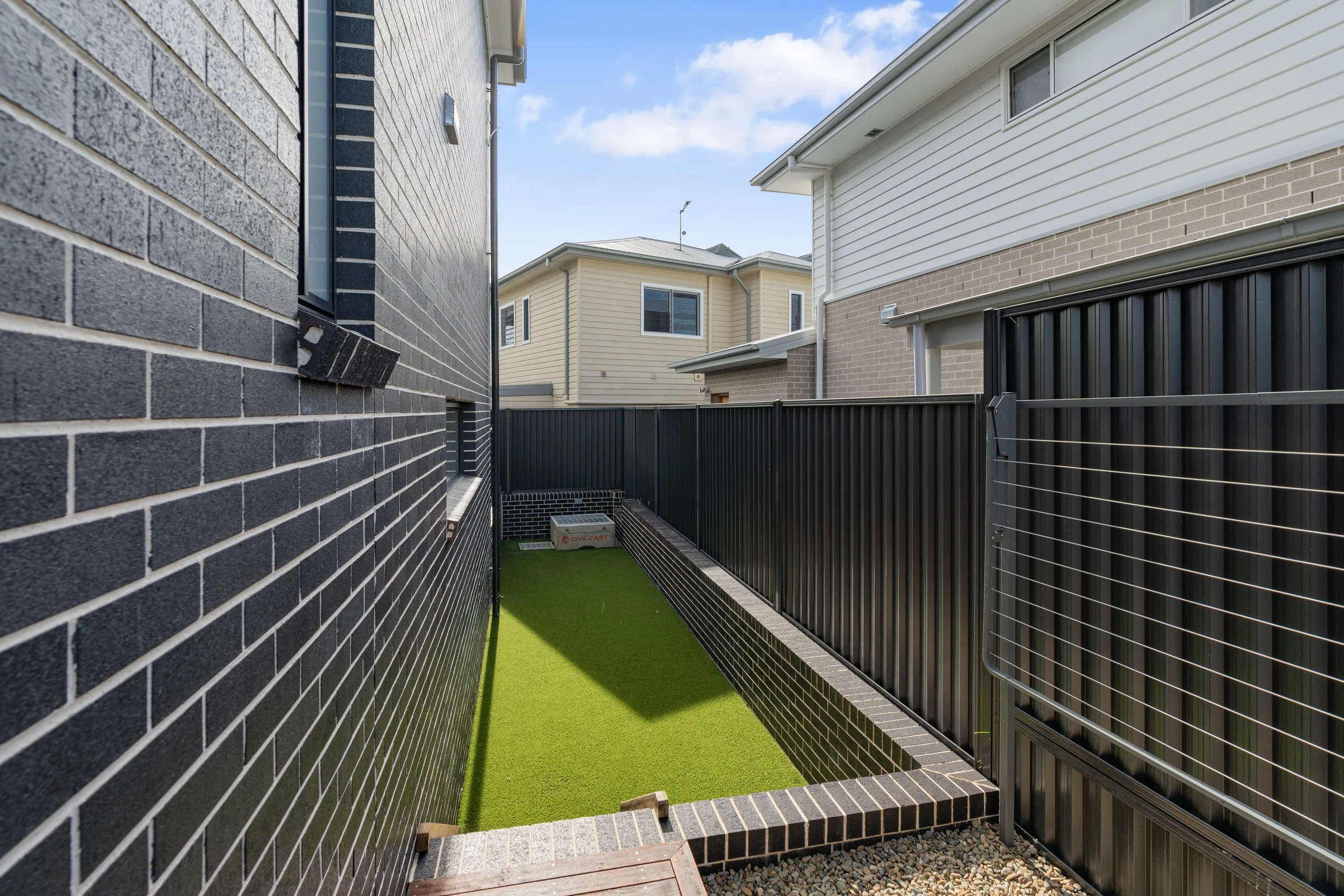 Turfed side yard between dark brick and new boundary fencing, Seven Hills
