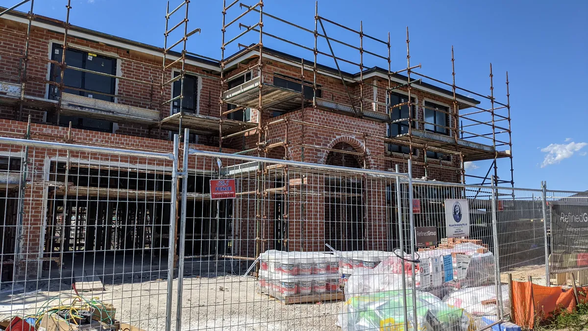 Brickwork, scaffold and site fencing on a two storey home being built by Refined Group